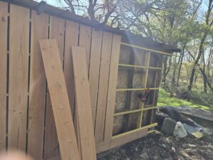 Bardage vertical en bois clair sur une remise, le chantier est en cours. Ossature jaune et cloueur visibles, avec des planches de bois en attente.