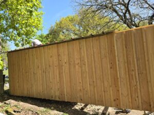 Long mur d'abri neuf en construction, composé de planches de bois verticales. Un ouvrier installe le toit métallique sous un ciel bleu.