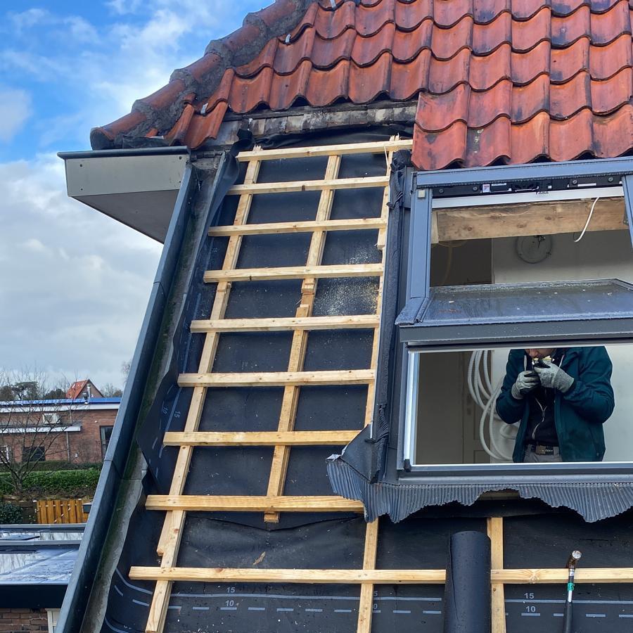Rénovation de toiture: tuiles, membrane noire et lattis bois. Velux moderne installé, un ouvrier filme. Marquages '15, 10, 5'.