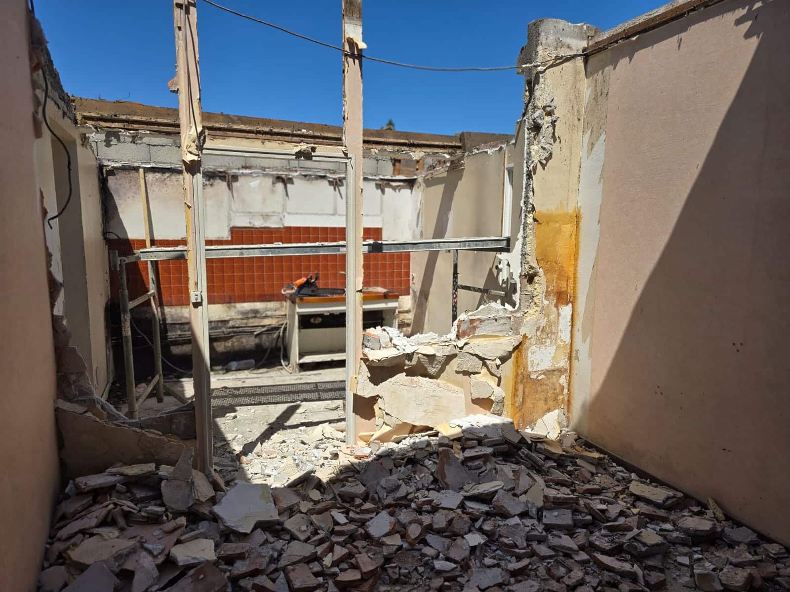 Chantier de démolition intérieure avec gravats au sol et murs cassés sous un ciel bleu.
