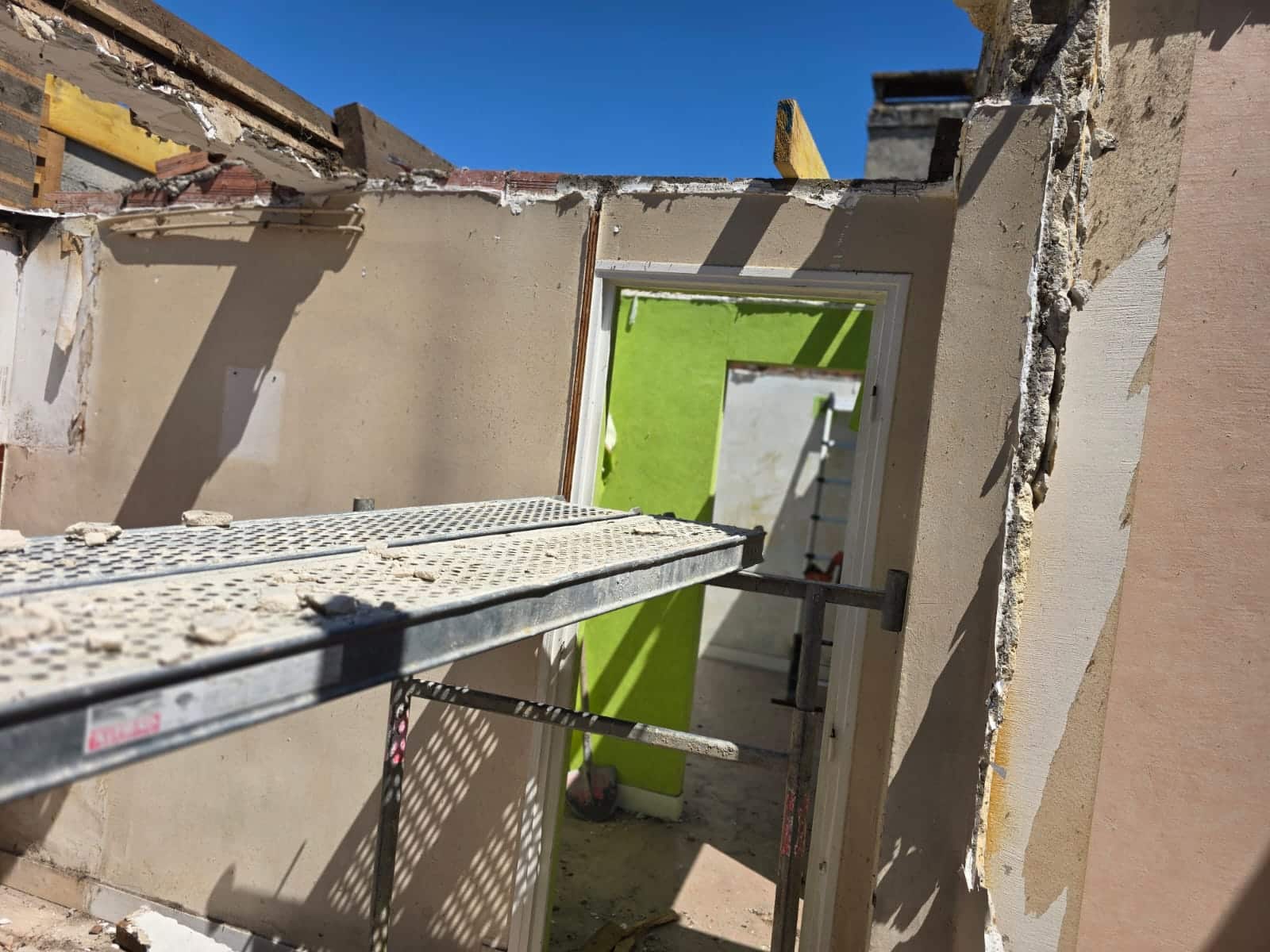 Chantier de rénovation avec échafaudage, murs en démolition et ciel bleu visible à travers le toit ouvert.