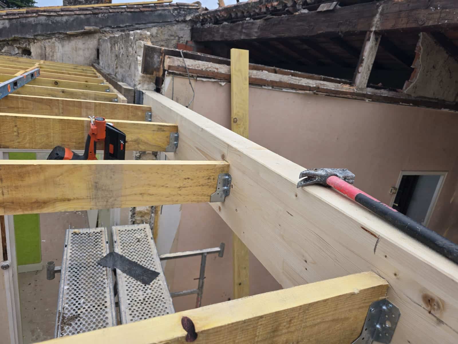 Pose de solives en bois avec sabots de fixation et cloueuse sur un chantier de rénovation.