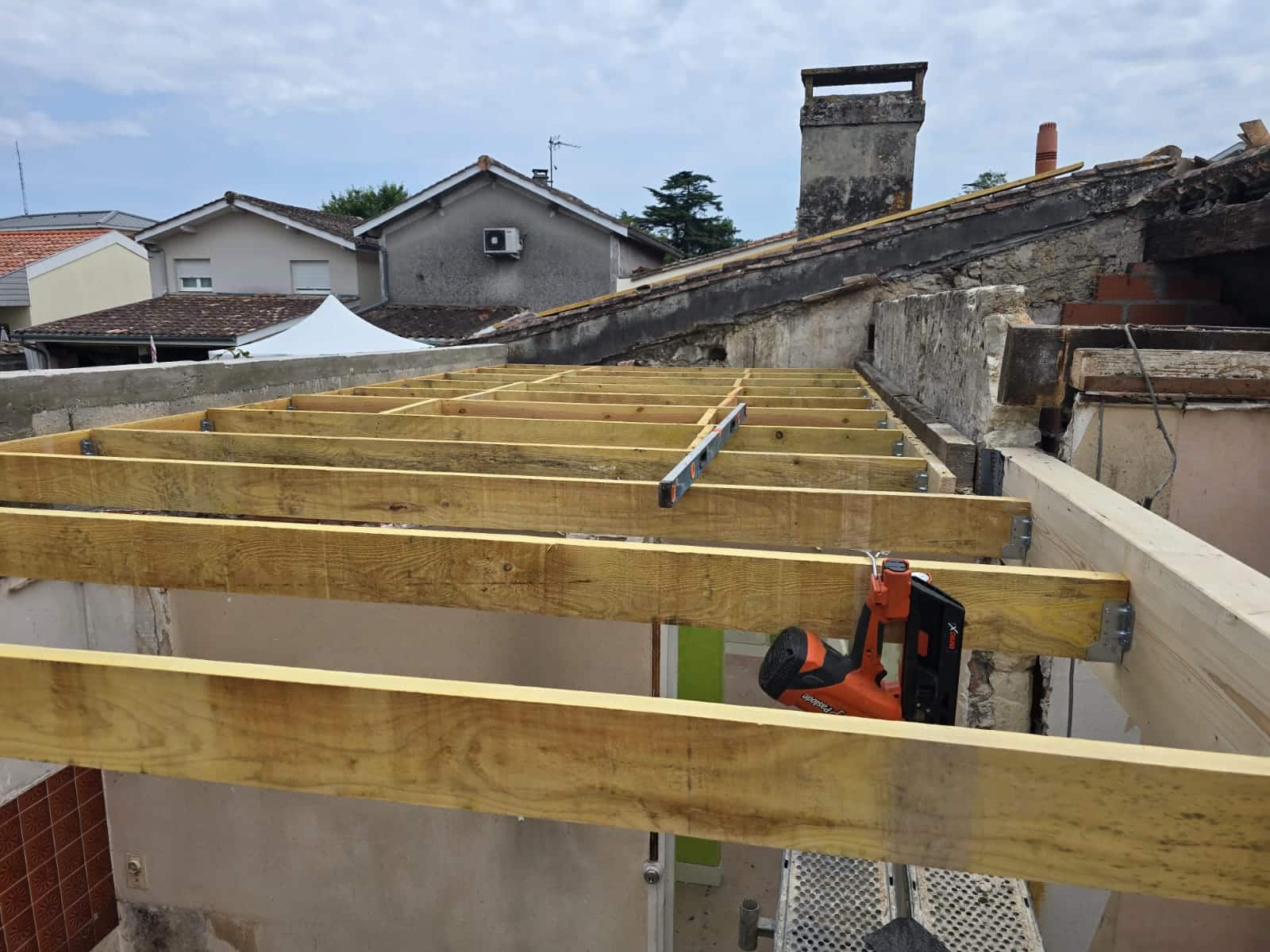 Installation de solives en bois pour une charpente de toiture avec un cloueur Paslode sur le chantier.