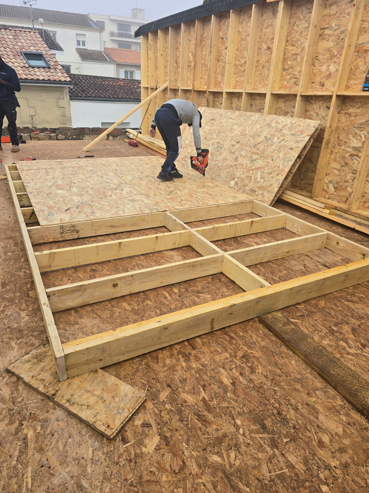 Ouvrier fixant des panneaux OSB sur une ossature bois avec un pistolet cloueur sur un chantier de construction.
