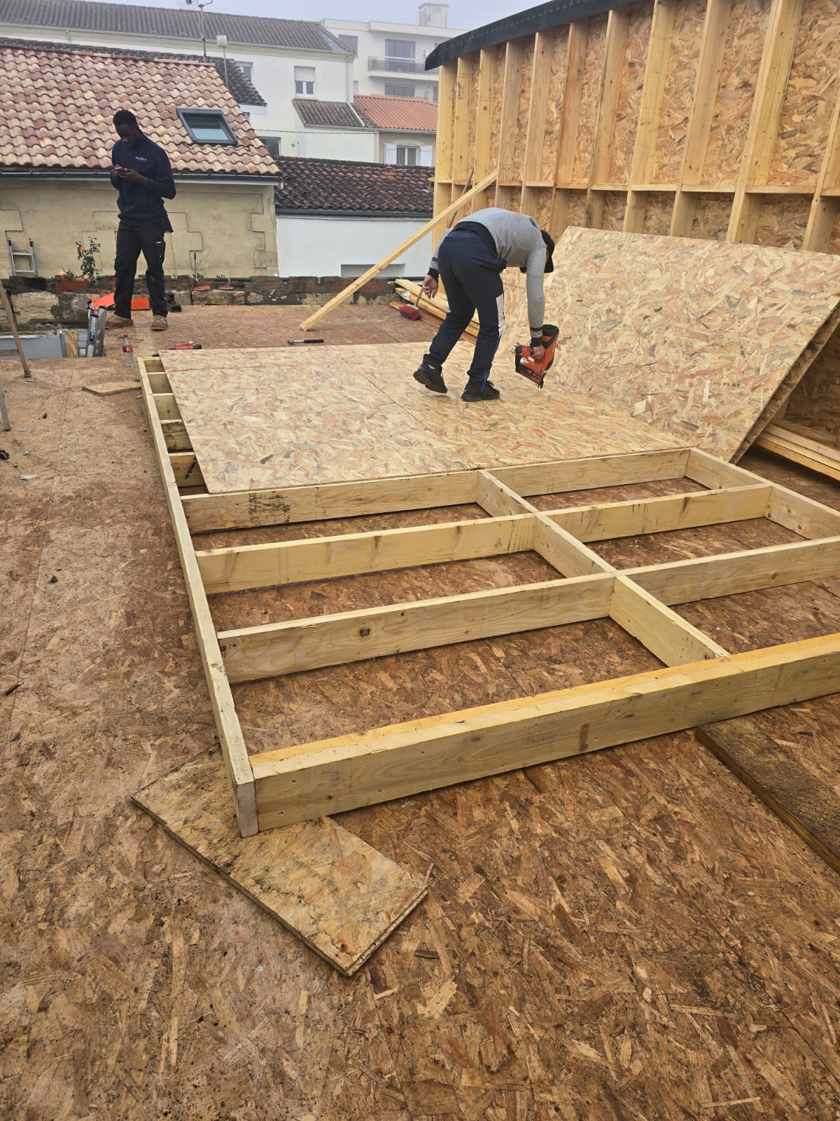 Ouvrier utilisant une cloueuse sur des panneaux OSB pour une construction en ossature bois sur un toit.