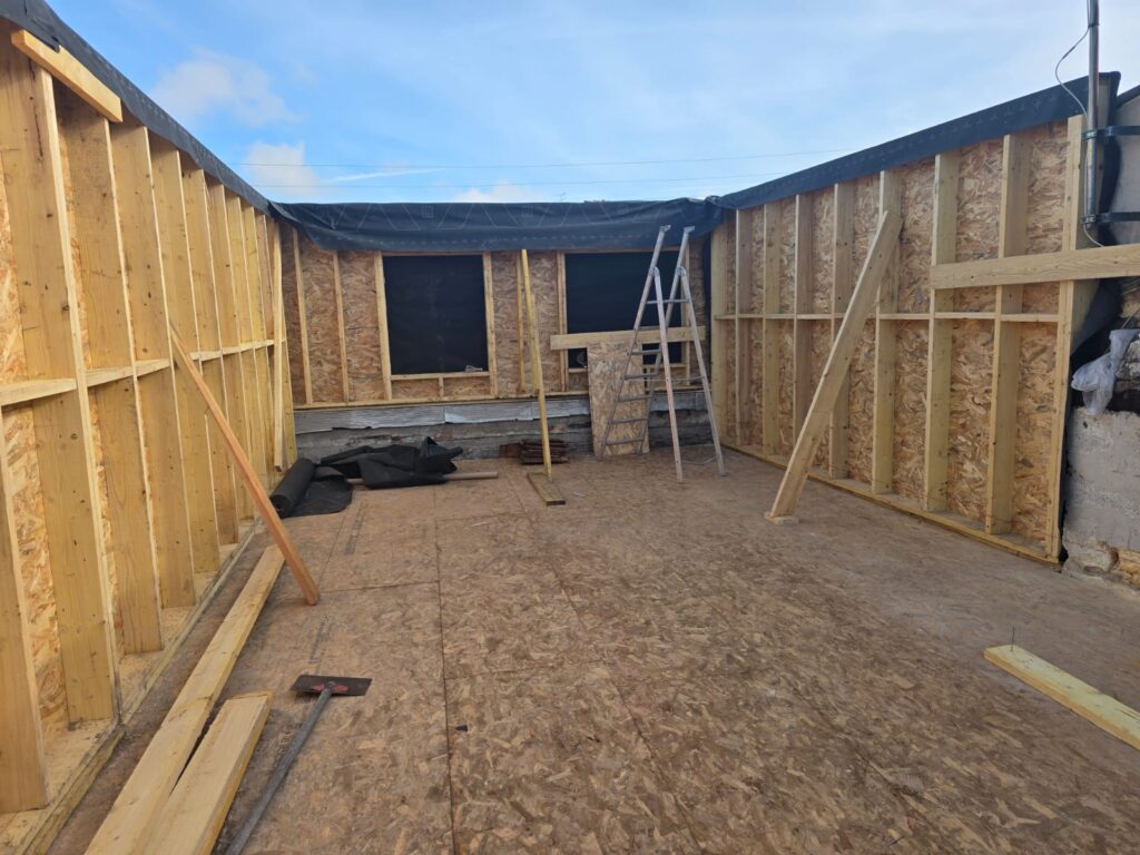 Chantier d'extension en ossature bois avec murs porteurs, plancher en OSB et ouvertures de fenêtres sous ciel bleu.