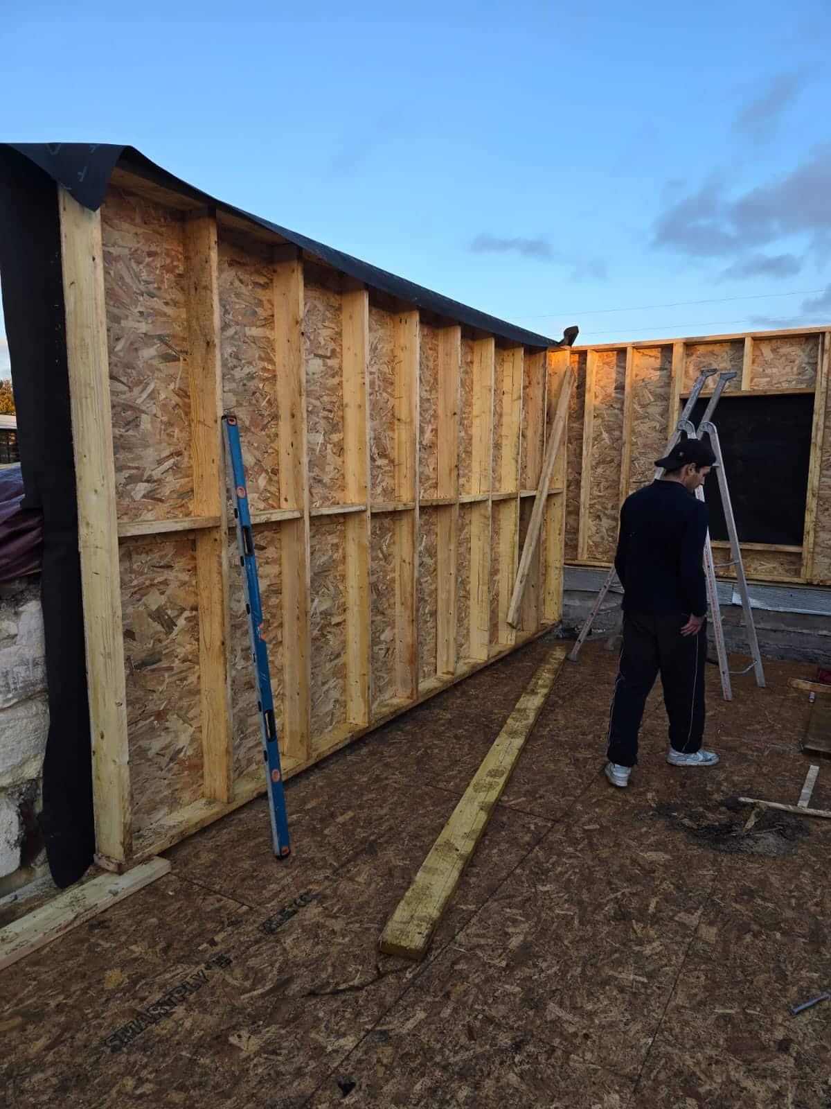 Ouvrier sur un chantier de construction bois avec murs en OSB et montants de charpente apparents.