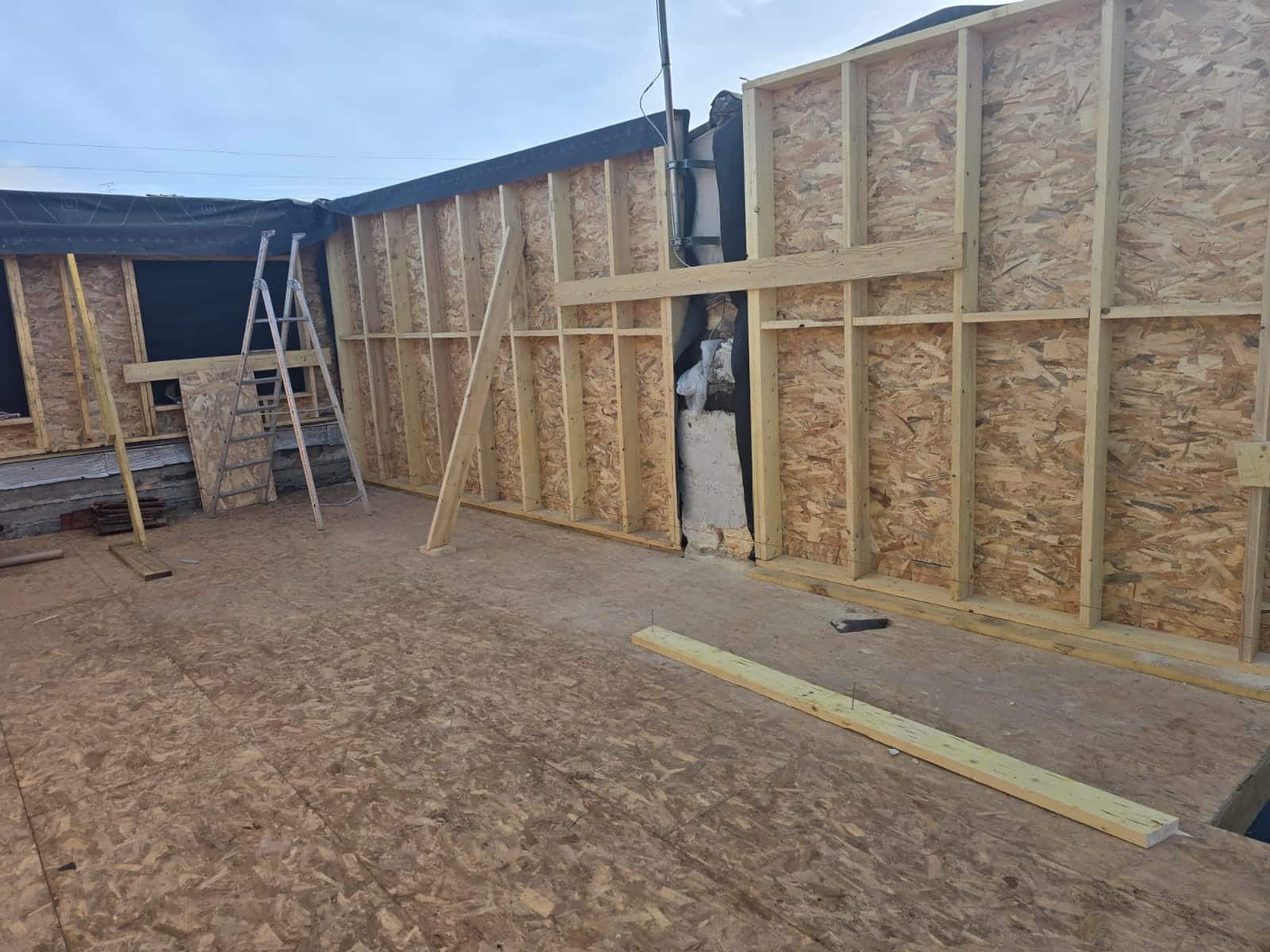 Structure en bois d'une extension de maison avec murs en OSB et montants de charpente sur un plancher bois.