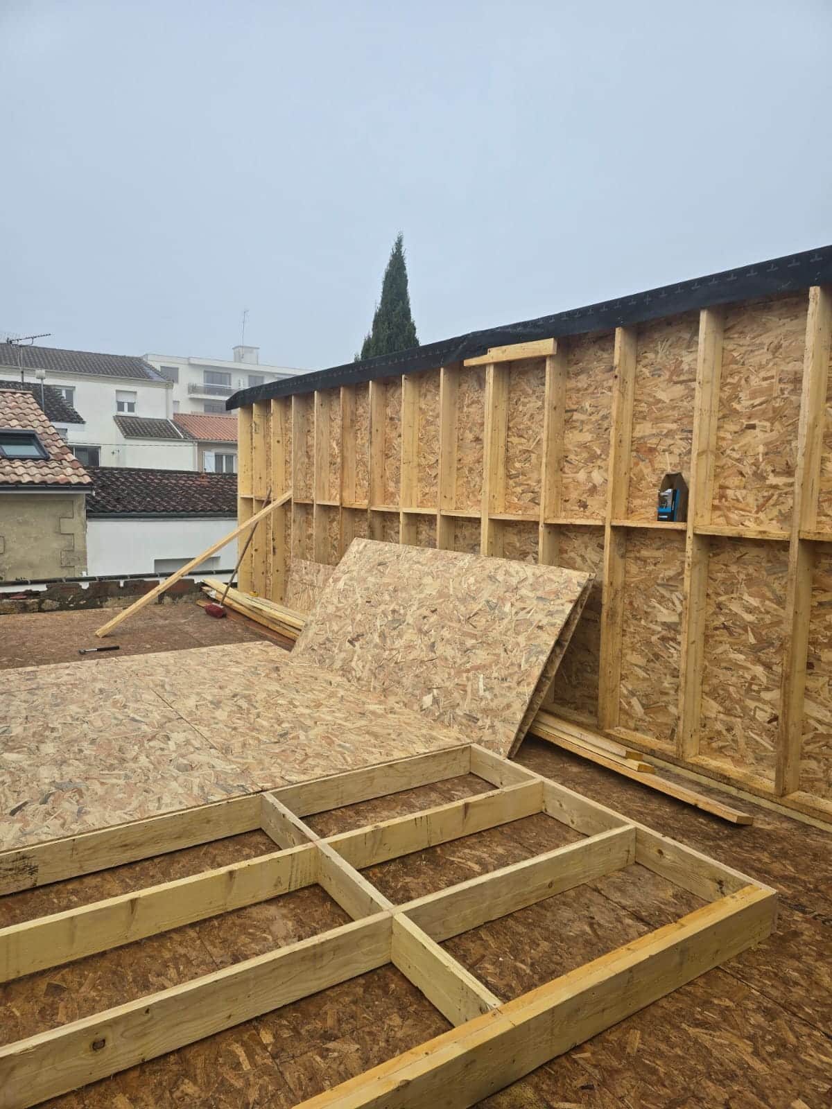 Structure de mur et plancher en bois avec panneaux OSB sur un chantier de construction urbain.