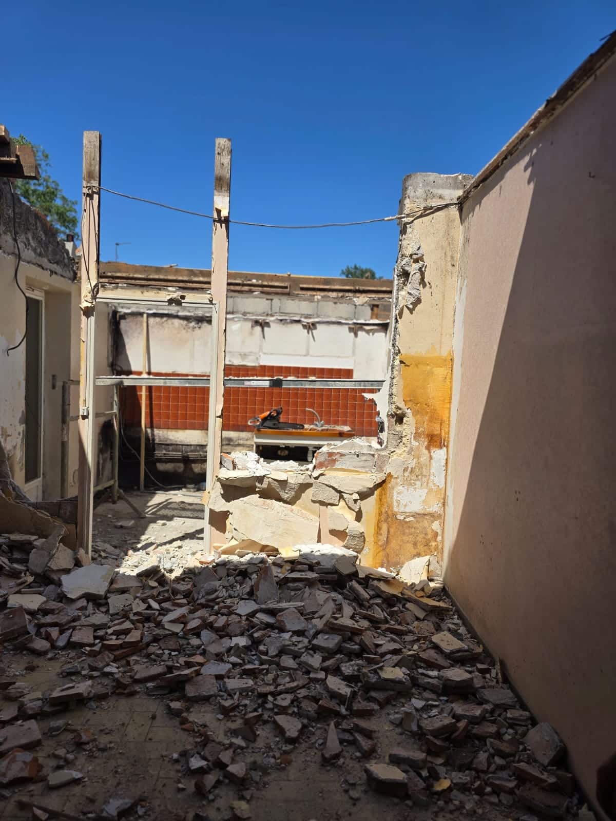Chantier de démolition d'une maison avec tas de gravats au sol et murs en ruine sous le soleil.