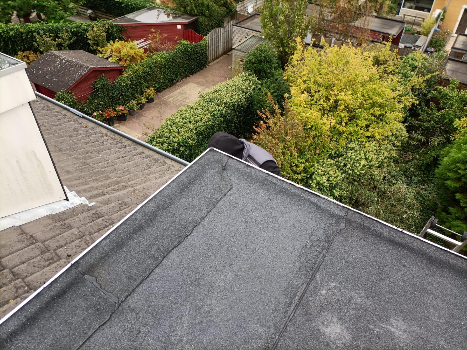 Couvreur travaillant sur une toiture plate en bitume avec bordures métalliques au-dessus d'un jardin.