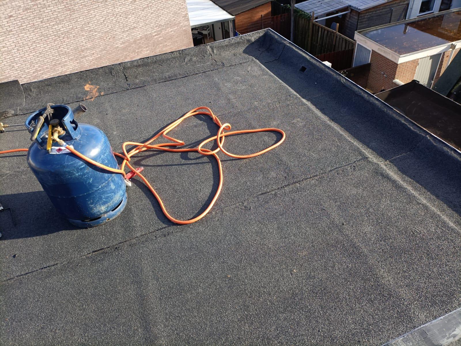 Bouteille de gaz propane sur un toit plat en bitume noir lors de travaux d'étanchéité de toiture.