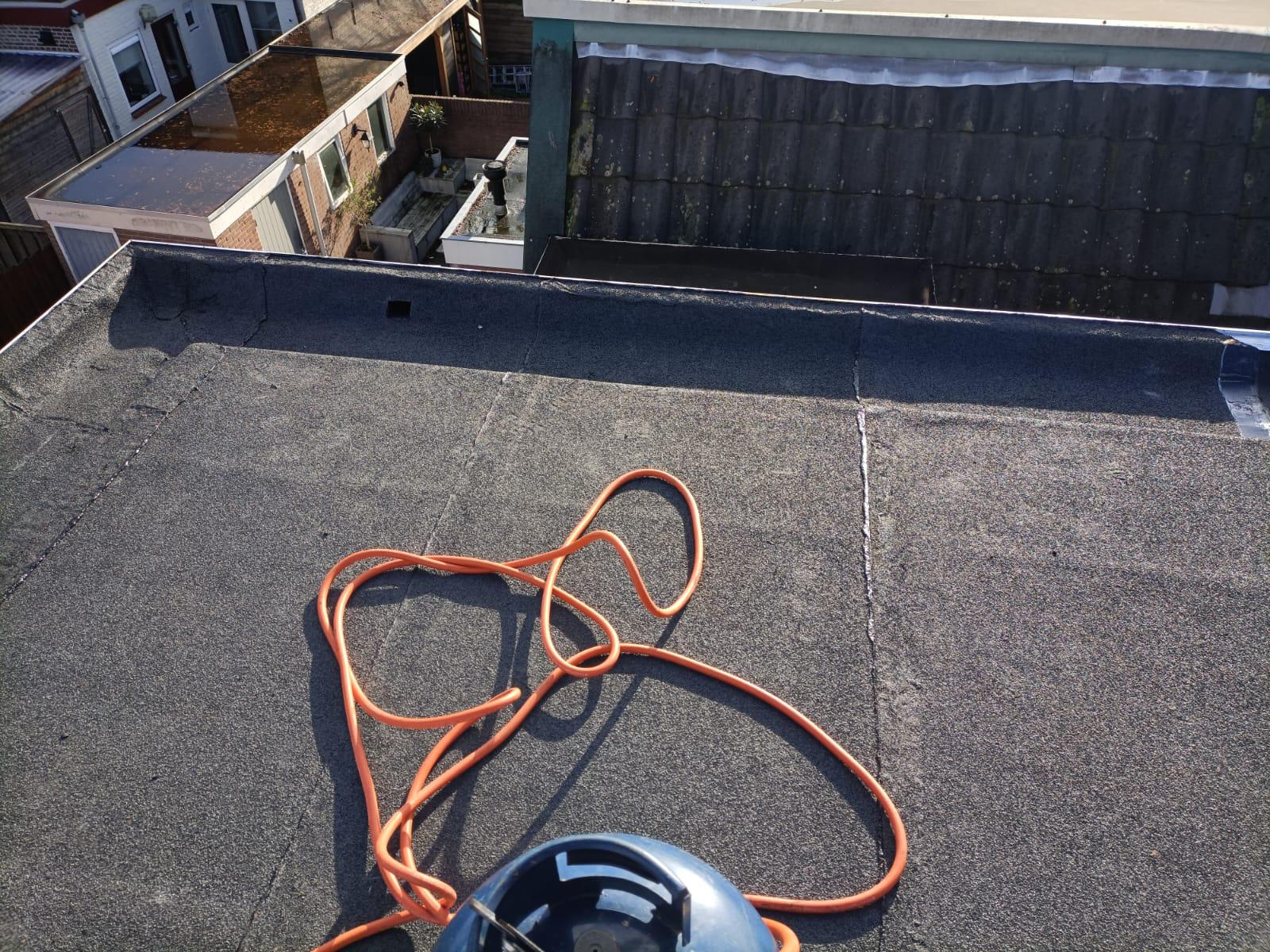 Étanchéité de toiture terrasse avec membrane bitumineuse, tuyau orange et bouteille de gaz pour pose au chalumeau.