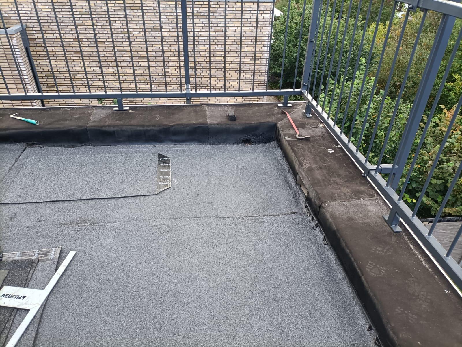 Étanchéité d'une toiture-terrasse avec membrane bitumineuse grise et installation d'un garde-corps métallique.