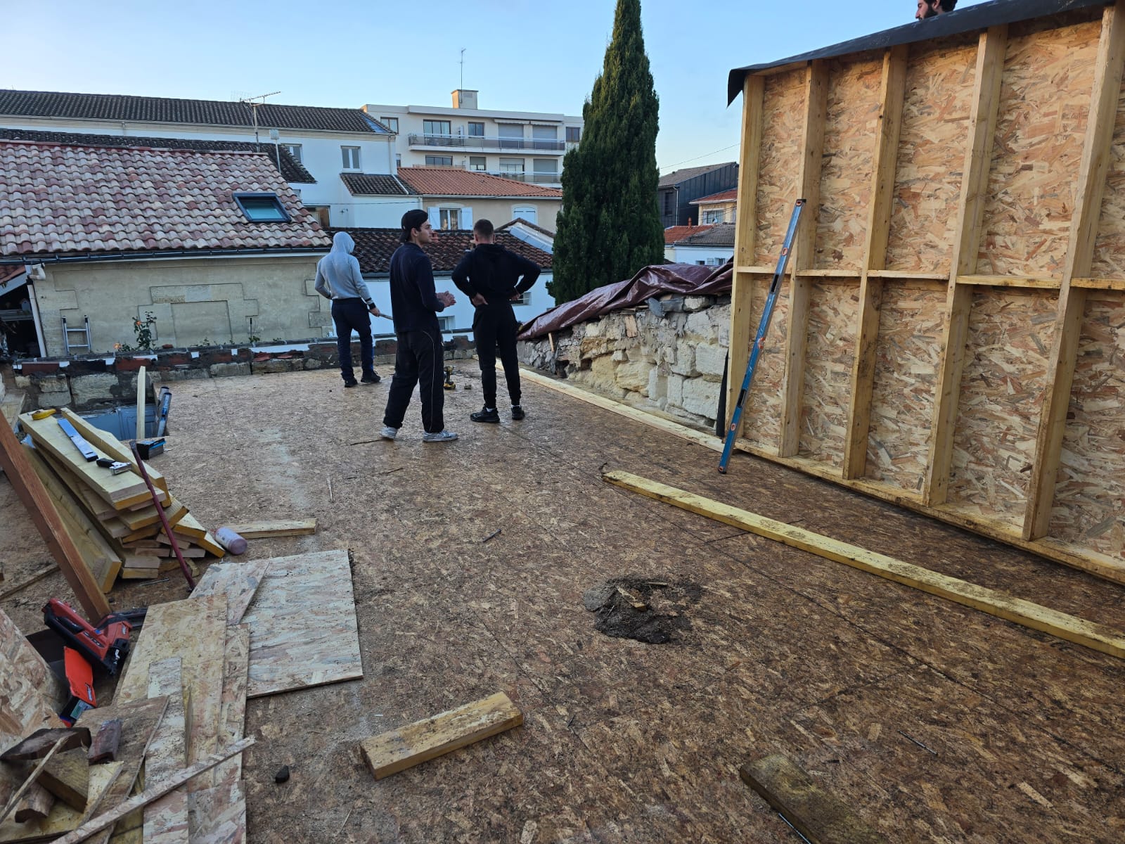 Ouvriers installant une ossature en bois sur une terrasse en panneaux OSB lors d'un chantier de rénovation.