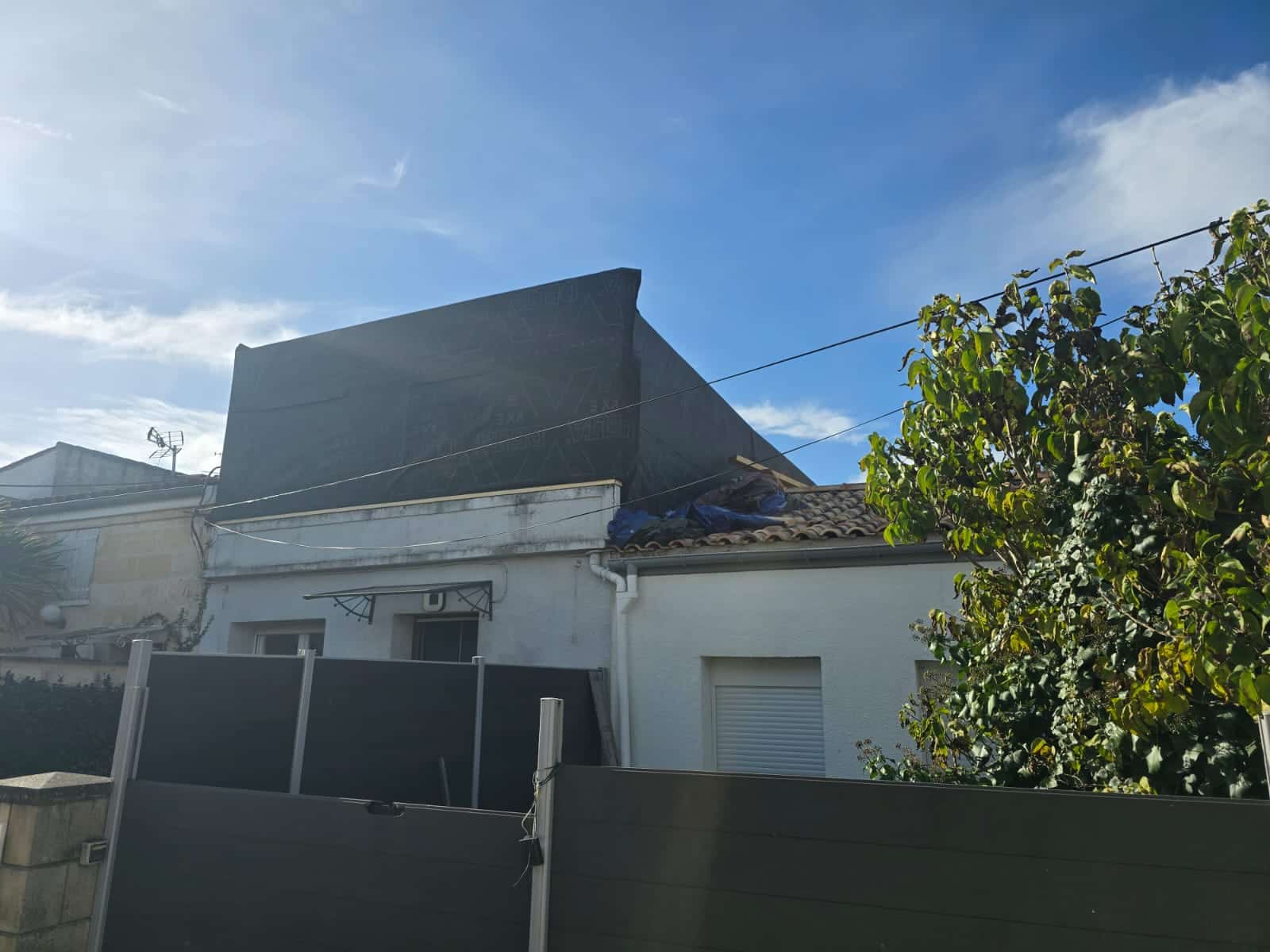 Extension de toiture protégée par une membrane noire Delta sur une maison blanche sous un ciel bleu.