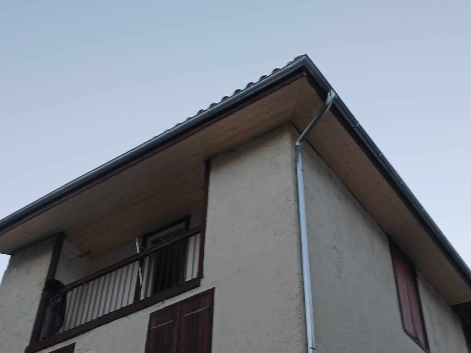 Angle de toiture avec gouttière en zinc, sous-face de toit en bois et balcon sur façade claire.