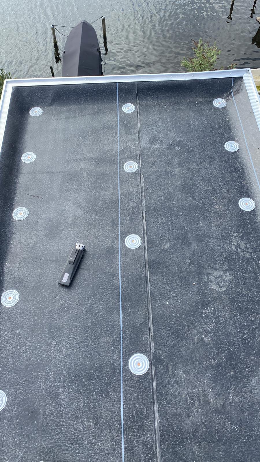 Installation d'une membrane de toiture plate noire avec attaches mécaniques circulaires et bordure en métal.