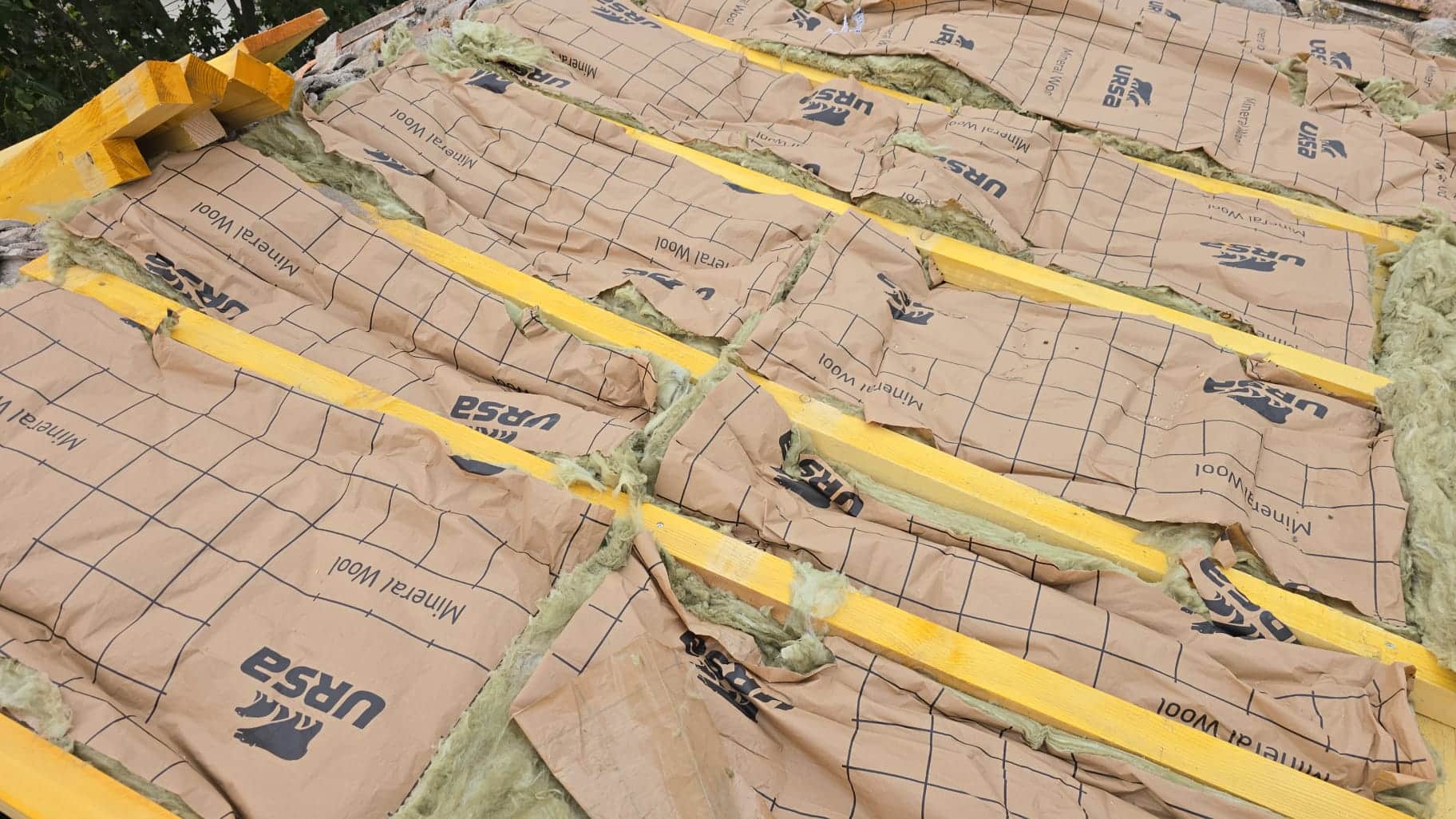 Pose de rouleaux d'isolant URSA Mineral Wool entre les solives en bois d'une charpente en cours de rénovation.