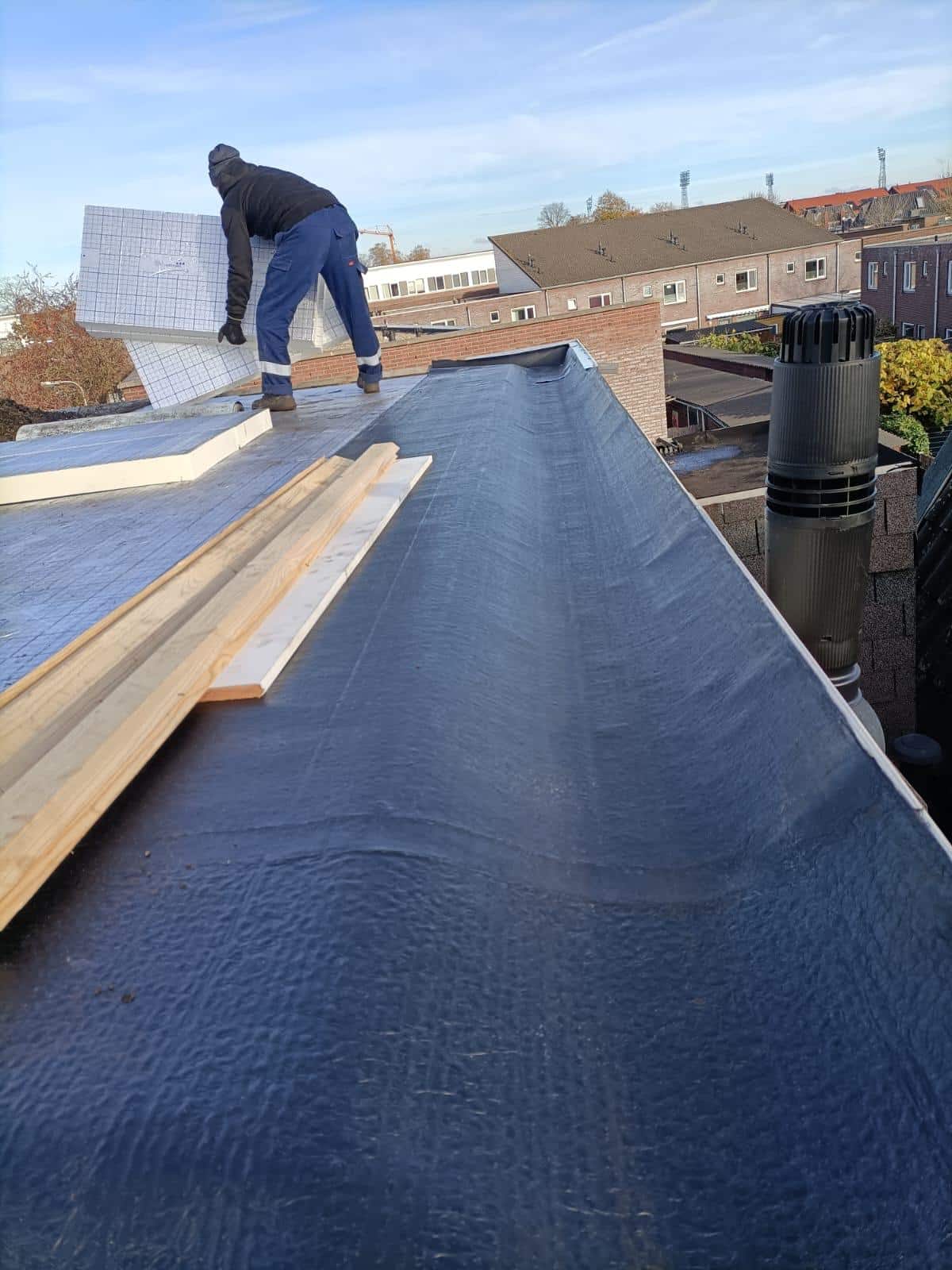 Ouvrier posant des panneaux isolants blancs sur une toiture plate avec membrane d'étanchéité noire.