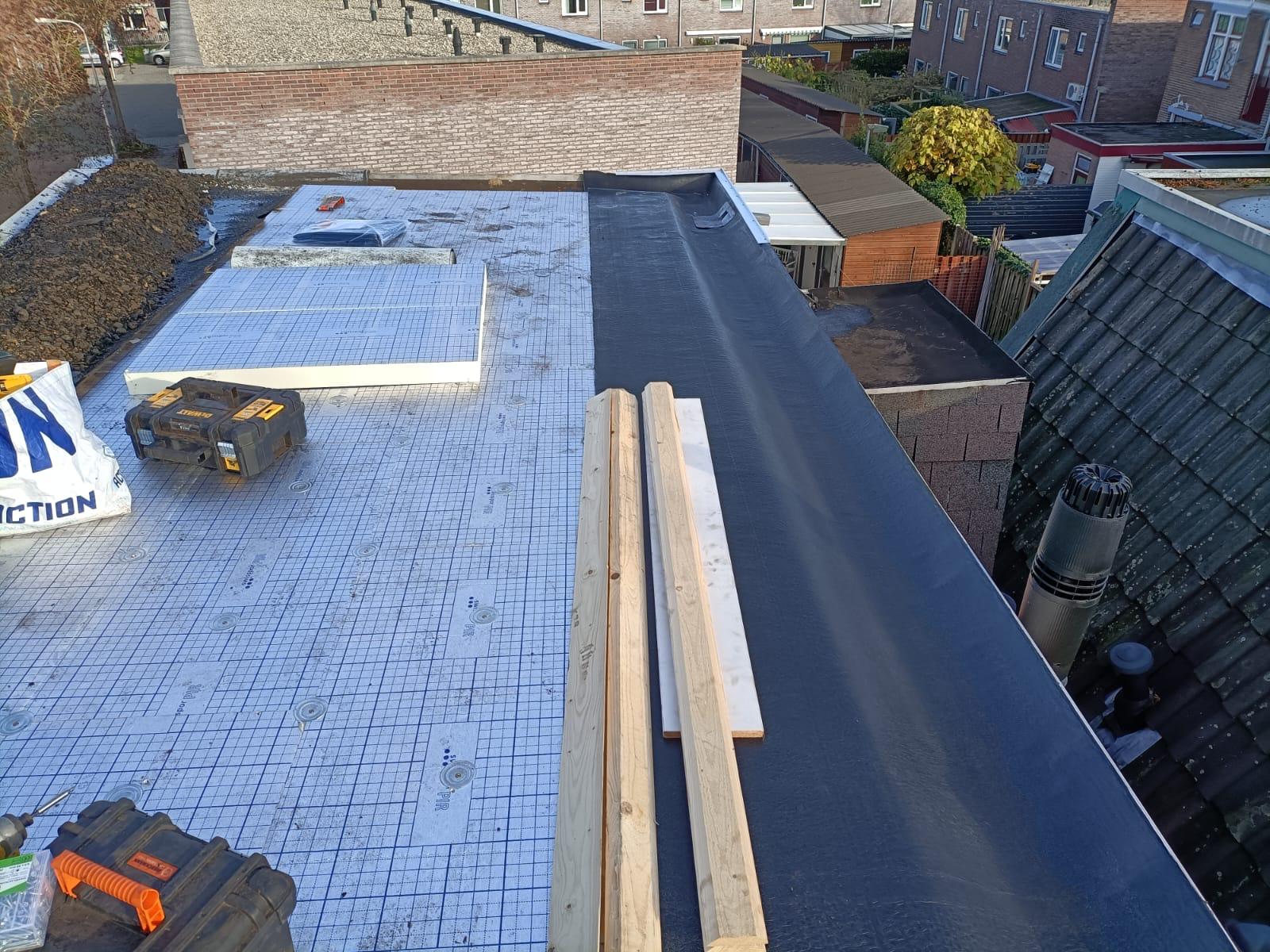 Installation d'isolant PIR et membrane d'étanchéité noire sur une toiture terrasse pendant des travaux de rénovation.