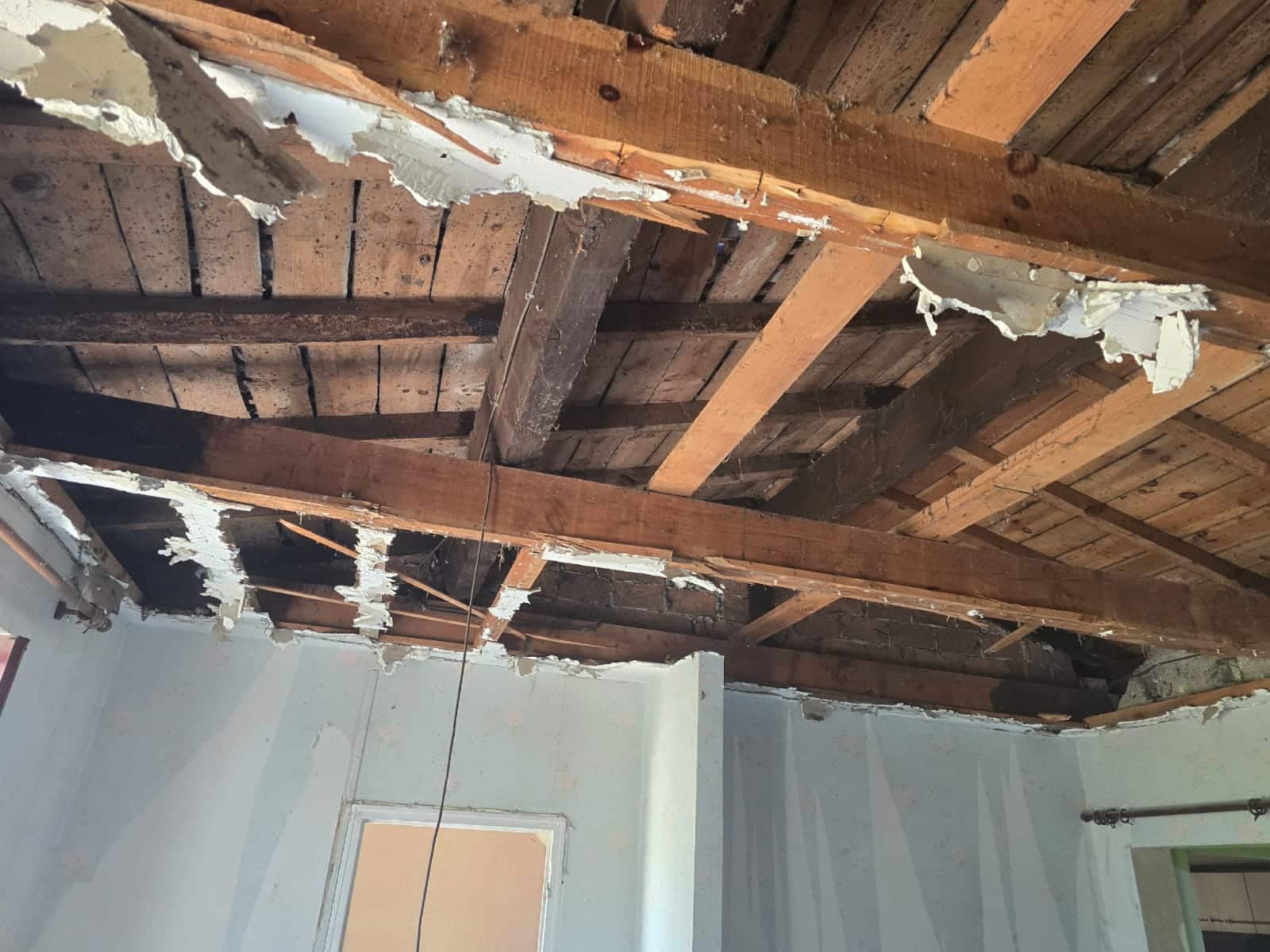 Plafond dégradé avec poutres bois apparentes et plâtre écaillé dans une pièce en cours de rénovation.