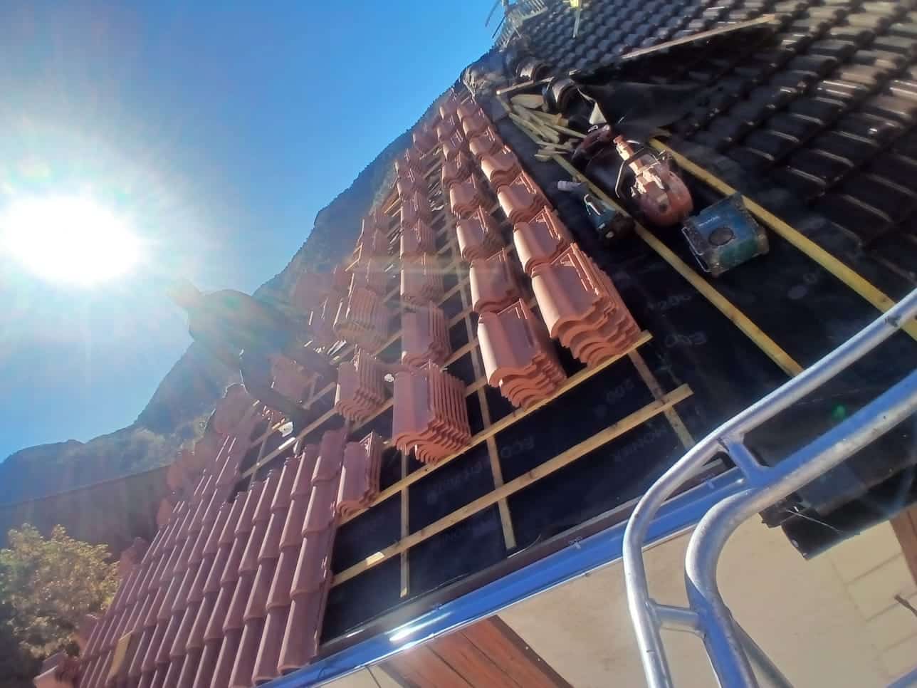 Couvreur installant des tuiles terre cuite Monier Ecotech 200 sur une charpente sous un soleil radieux.