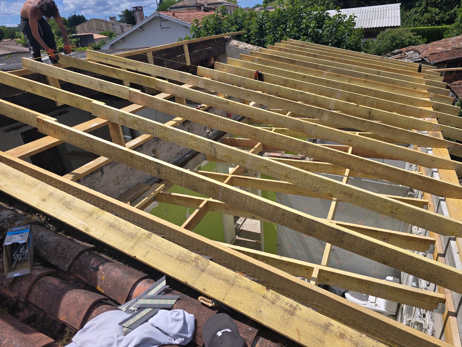 Charpente en bois en cours de rénovation avec un artisan fixant les chevrons sur le toit d'une maison.