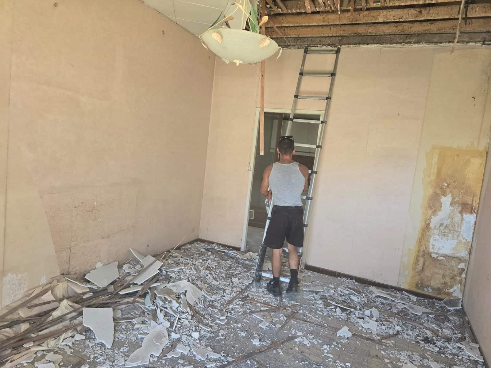 Ouvrier avec échelle télescopique dans une pièce en démolition jonchée de gravats et débris de plafond.