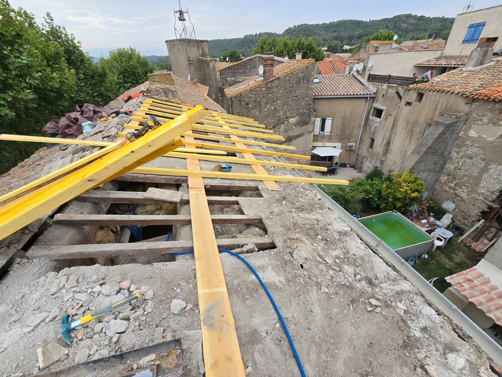 Rénovation de toiture avec poutres en bois jaune sur maison ancienne dans un village pittoresque.