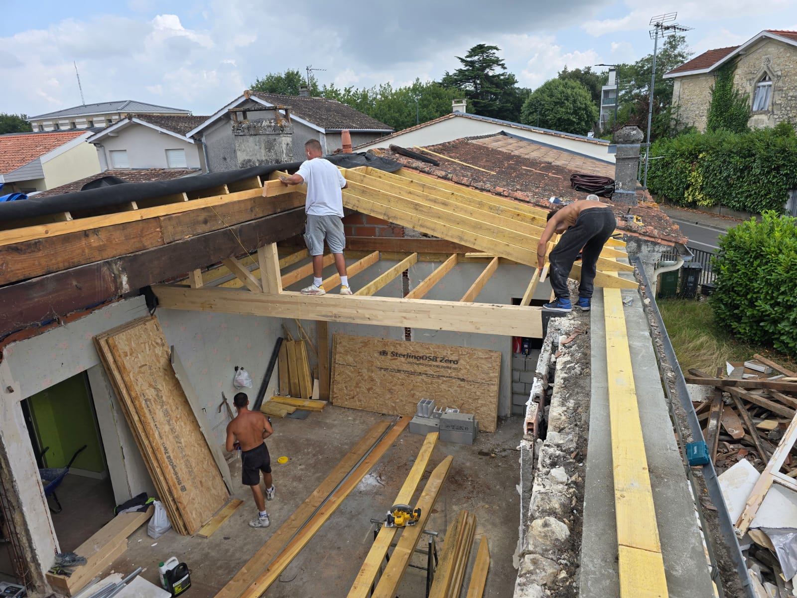 Ouvriers installant une charpente bois sur une maison en rénovation avec panneaux SterlingOSB Zero au sol.