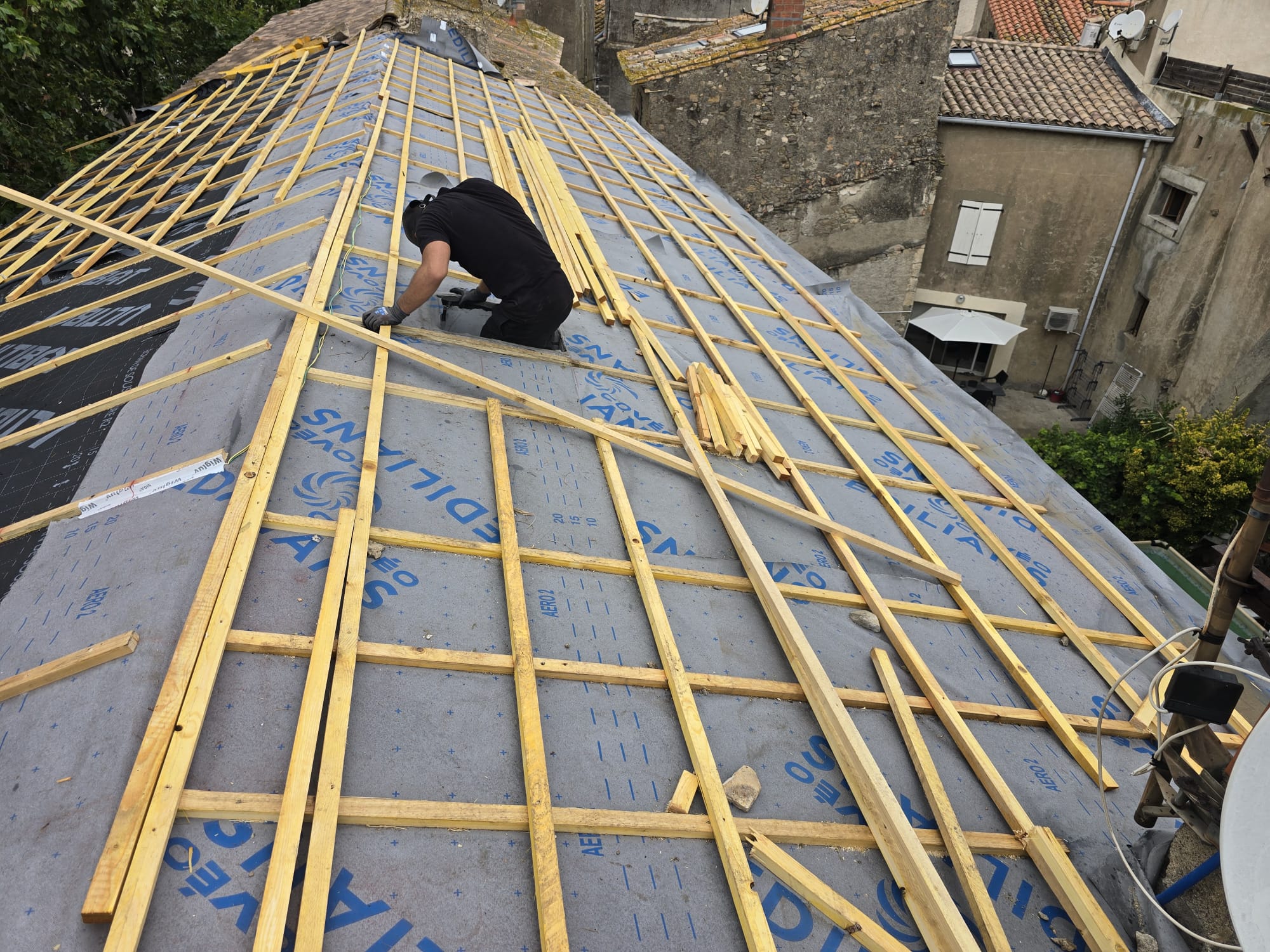 Couvreur installant des liteaux en bois sur écran de sous-toiture Edilians bleu lors d'une rénovation de toit.