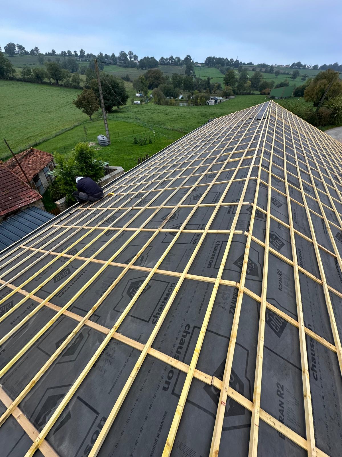 Ouvrier installant des liteaux sur un écran de sous-toiture Chausson Écran R2 lors d'une rénovation de toit en campagne.