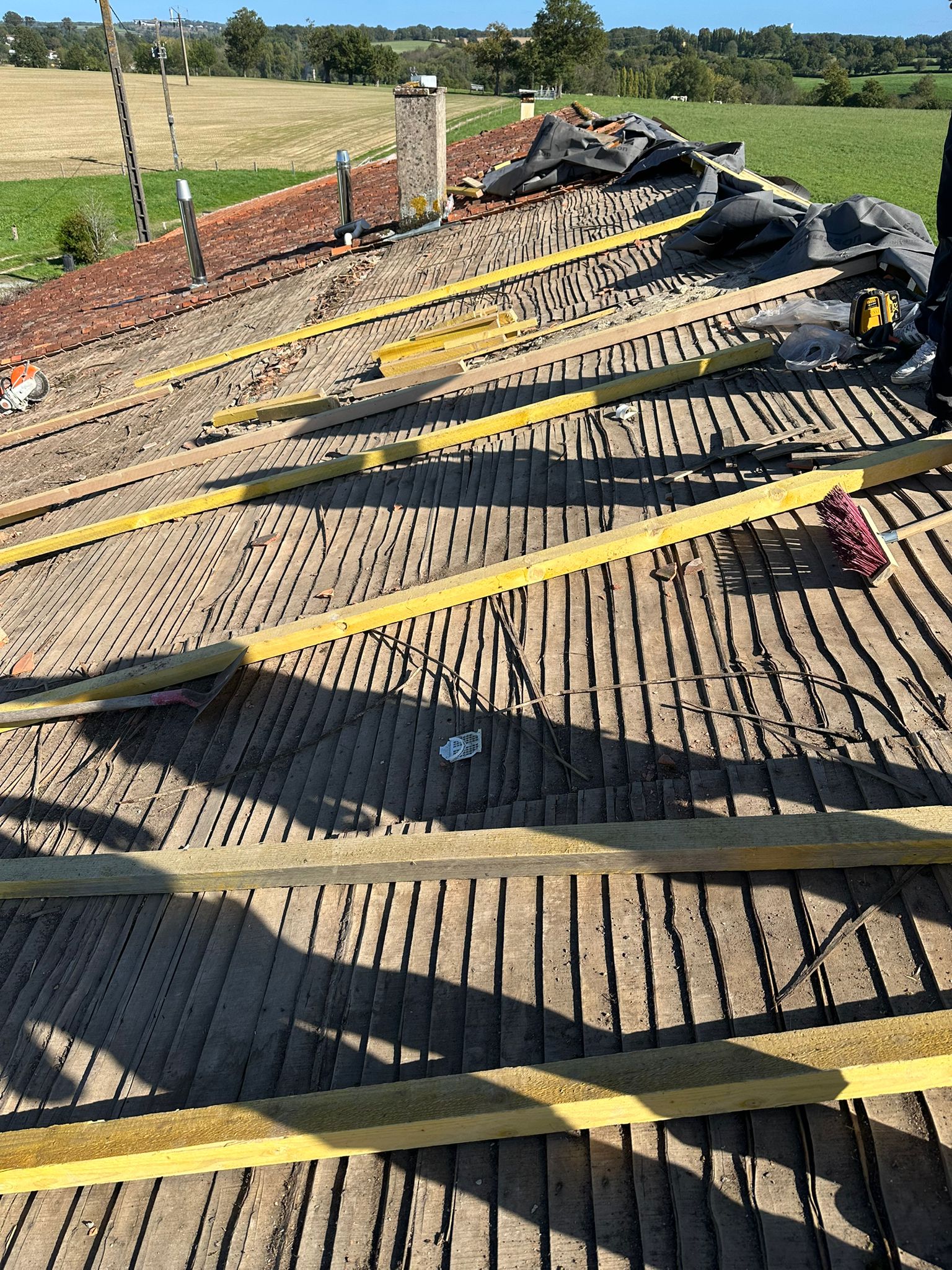 Chantier de rénovation de toiture avec pose de lattes en bois neuves sur une charpente ancienne à la campagne.