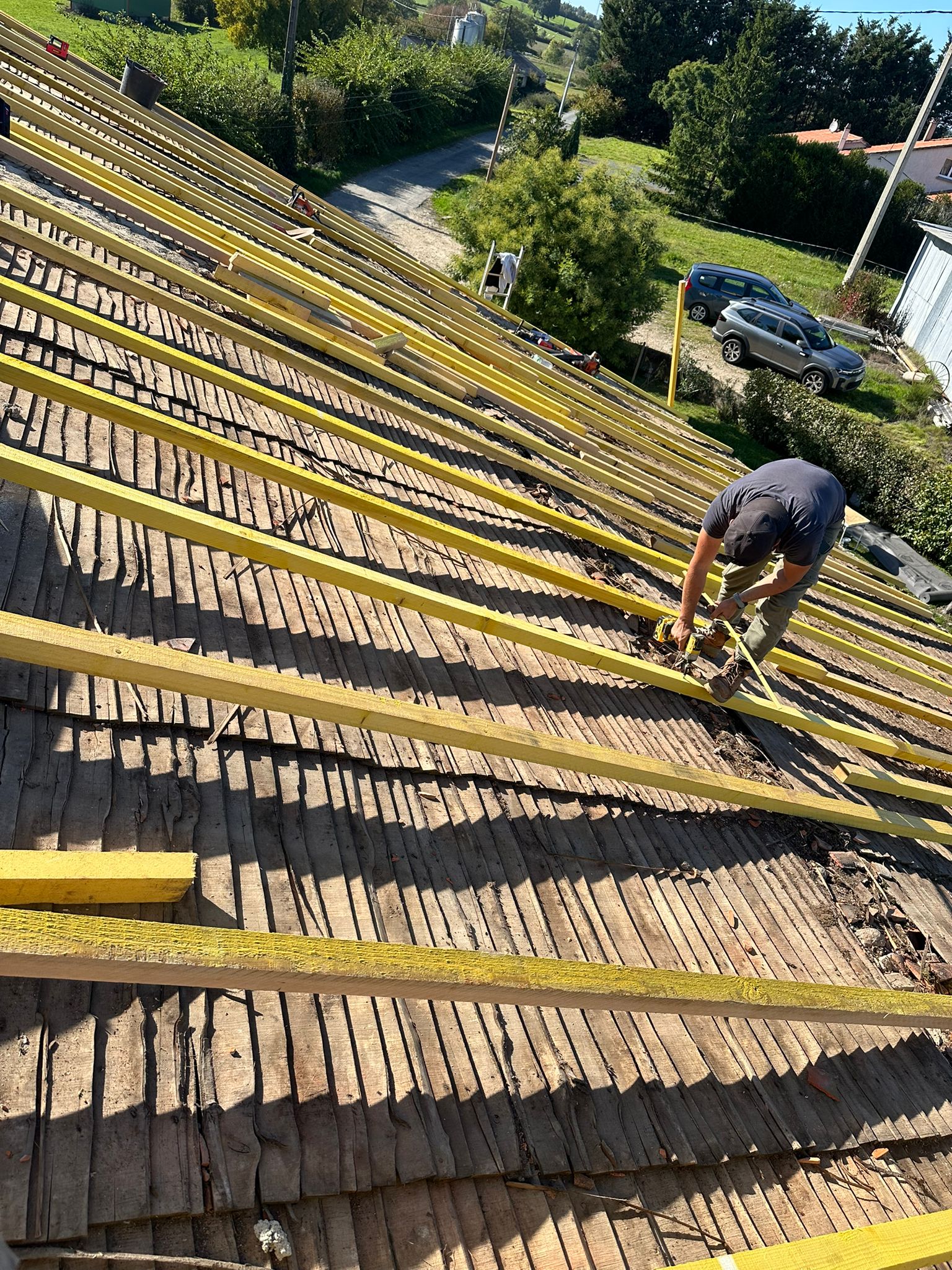 Couvreur installant des chevrons jaunes sur une toiture ancienne en bois lors de travaux de rénovation.