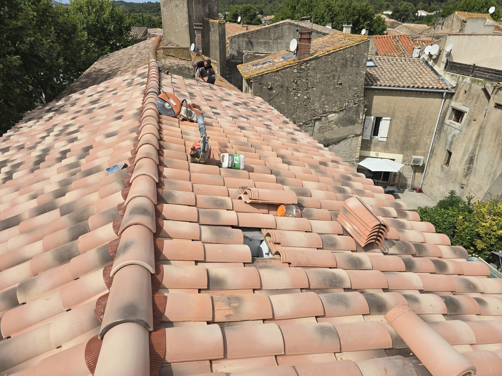 Artisan couvreur rénovant un toit en tuiles canal avec découpeuse thermique et bidon Marline sur un chantier de toiture.