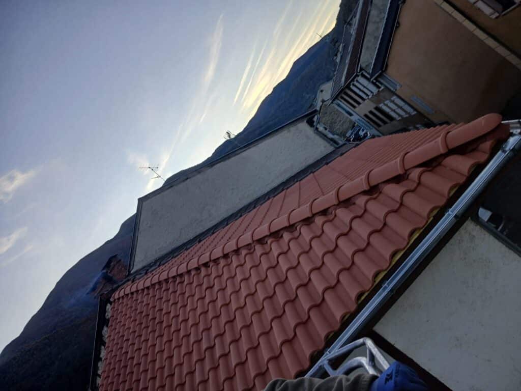 Toit en tuiles rouges devant des montagnes au crépuscule avec une échelle de chantier au premier plan.