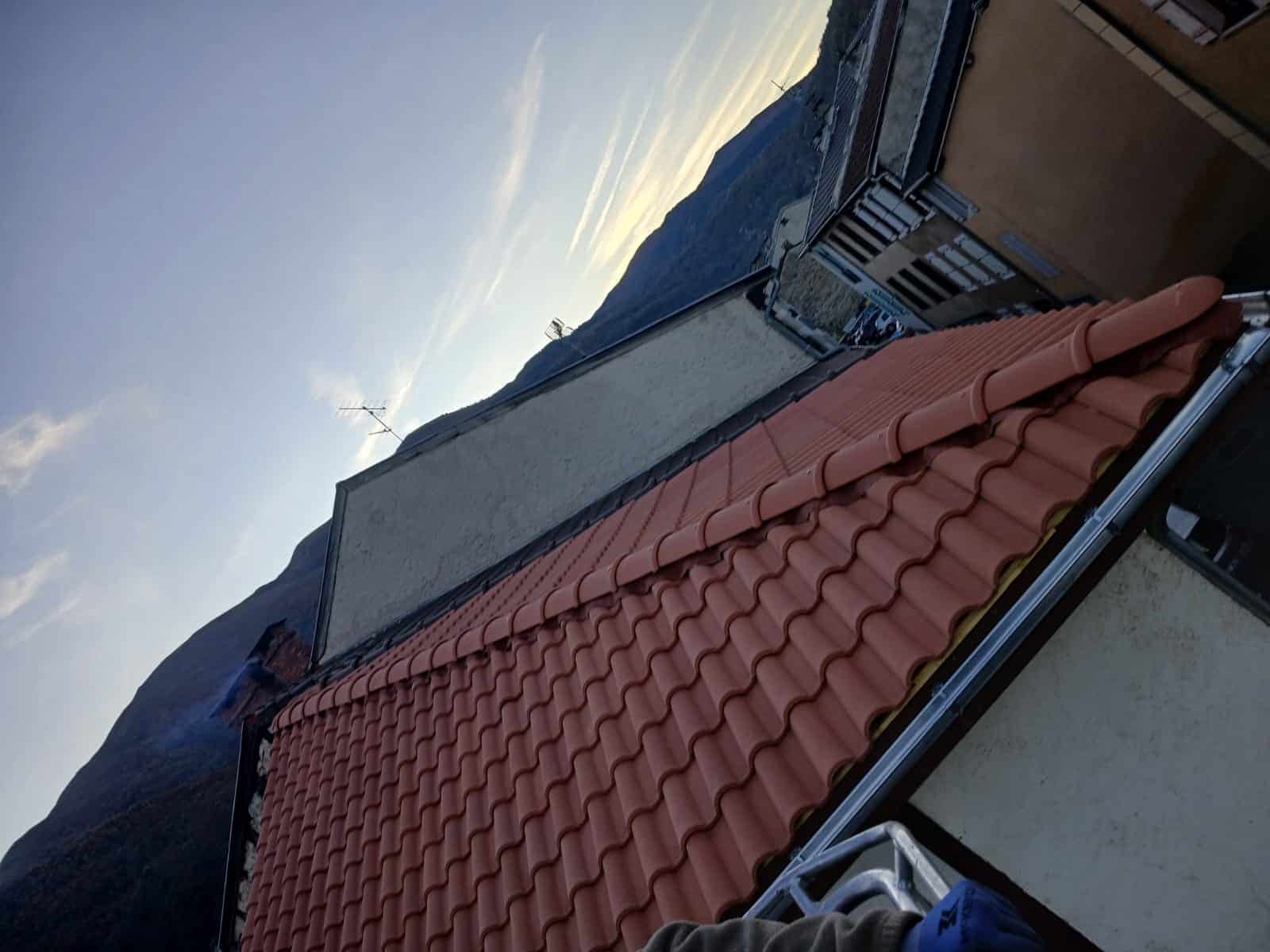 Toit en tuiles rouges devant des montagnes au crépuscule avec une échelle de chantier au premier plan.