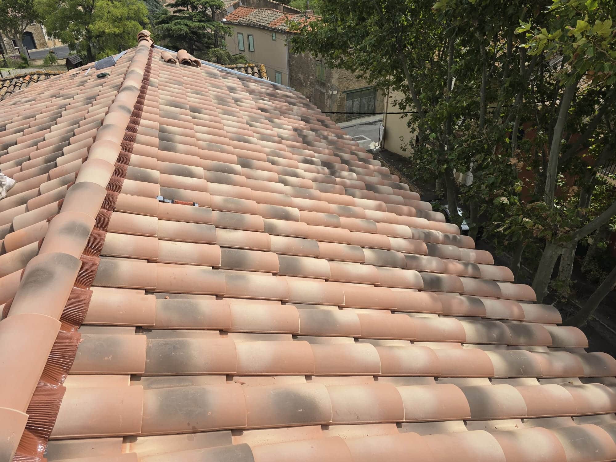 Toiture en tuiles canal terre cuite avec faîtage et closoir ventilé devant un paysage de village méditerranéen.