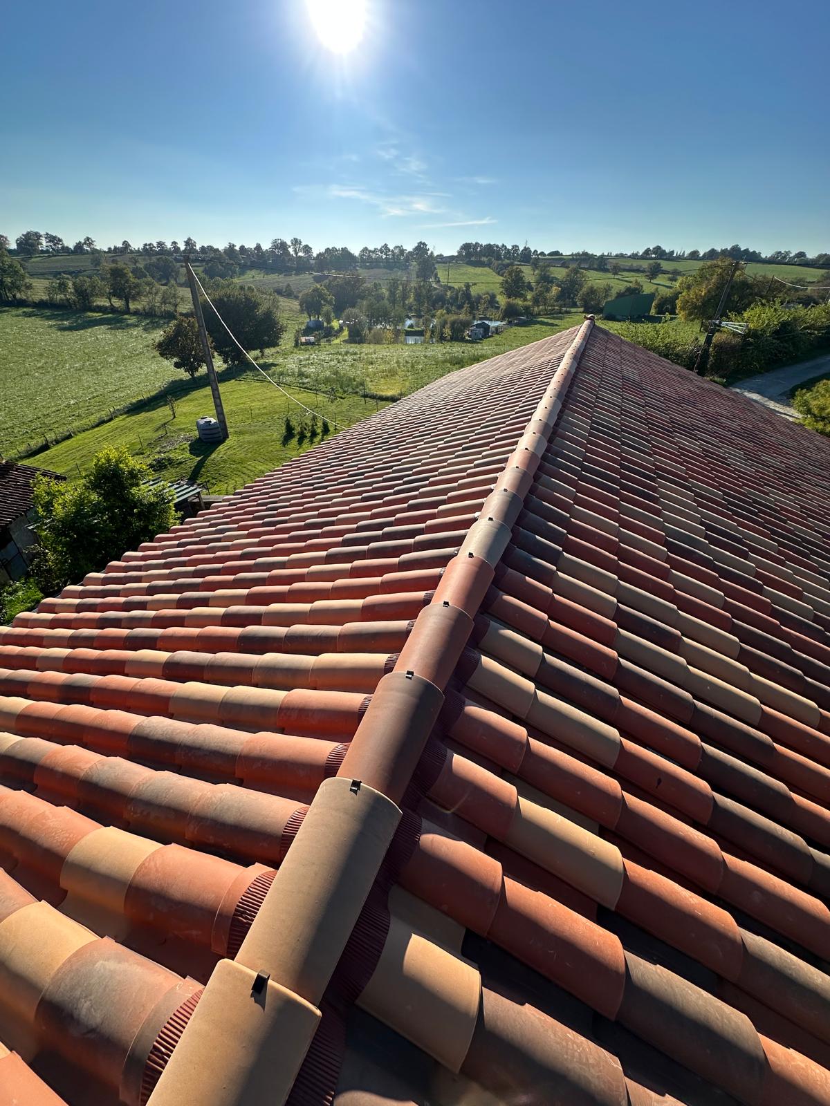 Toit en tuiles de terre cuite rouge sous un soleil éclatant avec vue sur une campagne verdoyante et vallonnée.