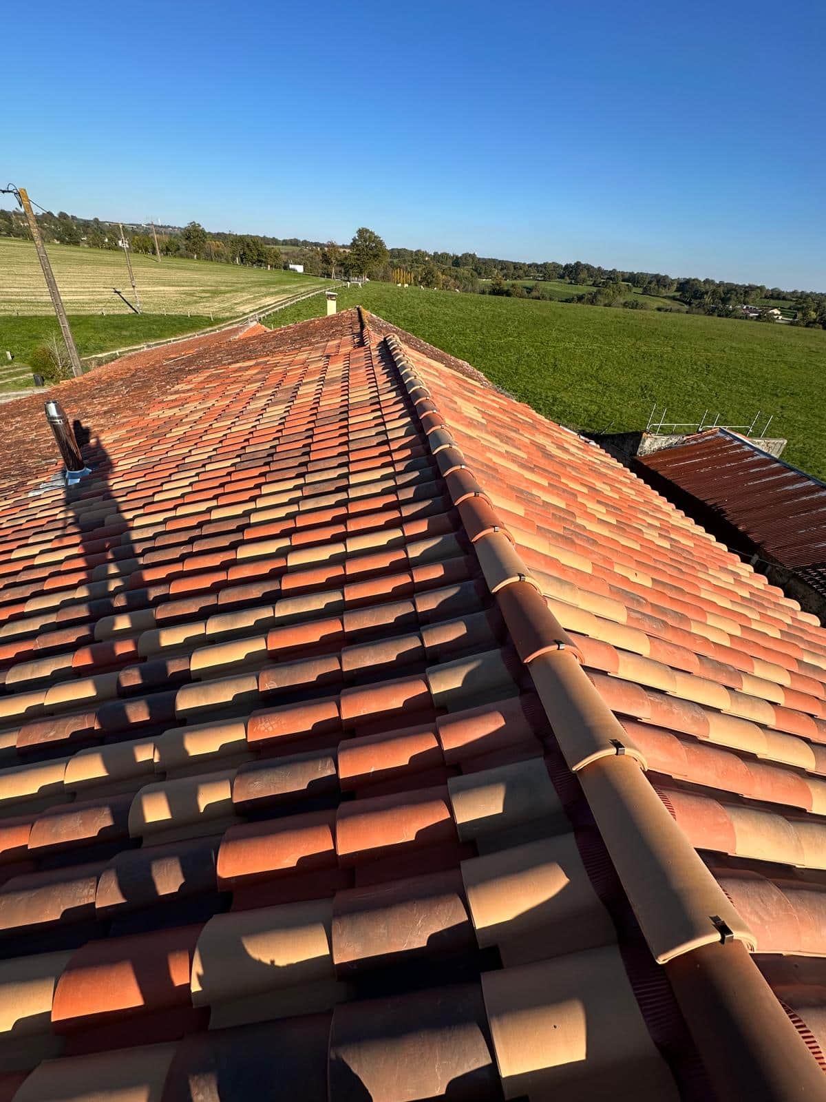 Toiture en tuiles canal de terre cuite sur une maison de campagne avec vue sur les champs verdoyants.